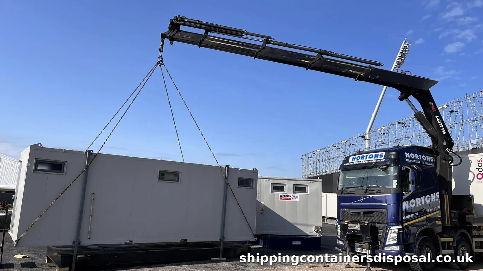 HIAB lorry lifting a grey portable cabin on chains beside a second unit