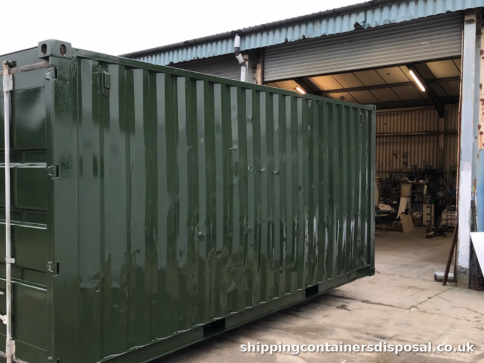 Side view of a refurbished dark green shipping container by a workshop door Side view of a refurbished dark green shipping container by a workshop door