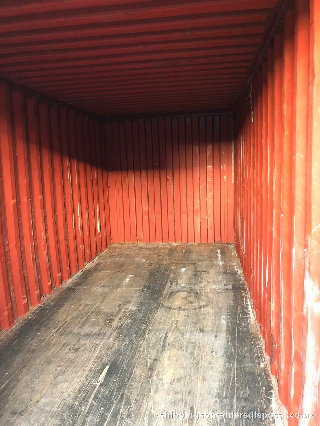 Worn interior of a red shipping container with a marked timber floor